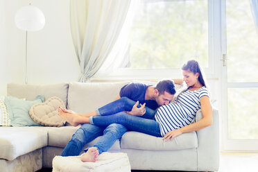 Man on sofa kissing pregnant woman's stomach - CUF05459