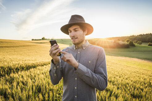 Mittlerer erwachsener Mann, im Feld stehend, Smartphone benutzend, Neulingen, Baden-Württemberg, Deutschland - CUF05467