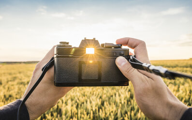 Mann steht im Feld, hält Spiegelreflexkamera, Sonnenlicht scheint durch den Sucher, Neulingen, Baden-Württemberg, Deutschland - CUF05474