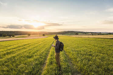 Mittlerer erwachsener Mann, im Feld stehend, Spiegelreflexkamera in der Hand, Blick auf die Landschaft, Neulingen, Baden-Württemberg, Deutschland - CUF05475