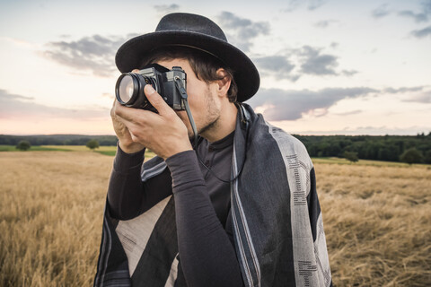 Mittlerer erwachsener Mann, stehend im Feld, fotografierend mit Spiegelreflexkamera, Neulingen, Baden-Württemberg, Deutschland, lizenzfreies Stockfoto