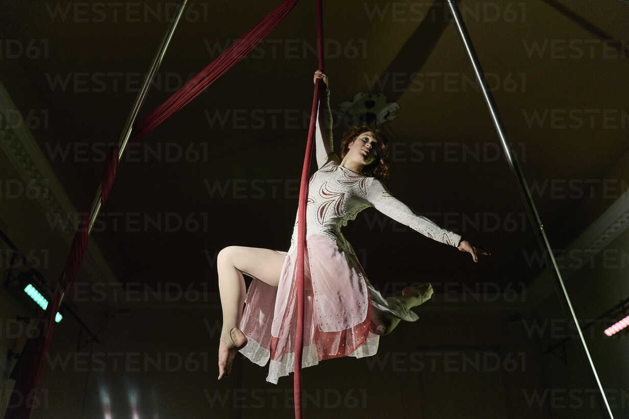 Low angle view of young female aerial acrobat hanging from silk