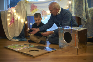 Boy and grandfather sitting on floor making robot costume - CUF05517