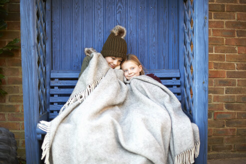 Geschwister in eine Decke gewickelt auf einer Laubenbank liegend - CUF05610