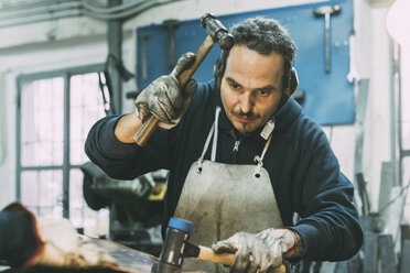 Male metalworker hammering metal in forge workshop - CUF05628