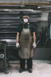 Portrait of male metalworker in dust mask, forge storeroom - CUF05632