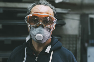 Portrait of metalworker in dust mask and safety goggles in forge workshop - CUF05646