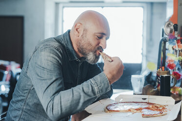 Älterer Mann, am Tisch sitzend, isst Pizza zum Mitnehmen - CUF05680