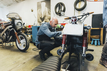 Älterer Mann, der in der Garage an einem Motorrad arbeitet - CUF05688