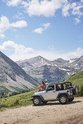 Road trip couple looking out at mountains from off road vehicle hood, Breckenridge, Colorado, USA - ISF01321