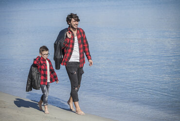 Vater und Sohn laufen am Strand entlang, tragen Jacken über der Schulter - ISF01326