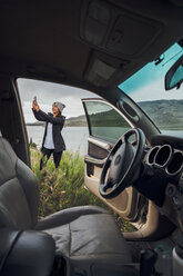 Junge Frau steht am Dillon Reservoir und hält ihr Smartphone, Blick durch ein geparktes Auto, Silverthorne, Colorado, USA - ISF01338