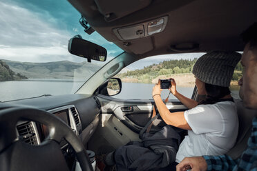 Couple in car, young woman taking photograph through car window, Silverthorne, Colorado, USA - ISF01340