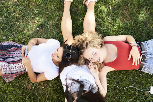 Drei junge Frauen liegen im Gras, telefonieren und hören Musik - IGGF00477