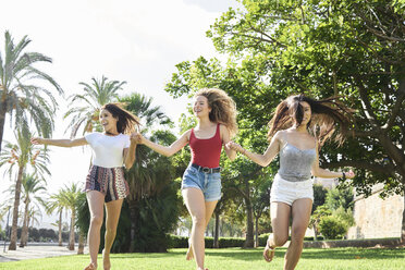 Spain, Mallorca, Palma, three happy young running holding hands together in a park in summer - IGGF00487