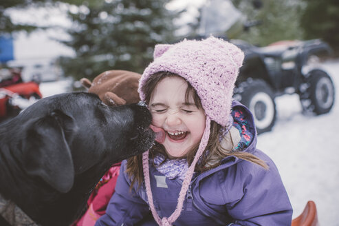 Junges Mädchen mit Hund in verschneiter Landschaft, Hund leckt das Gesicht des Mädchens - ISF01393