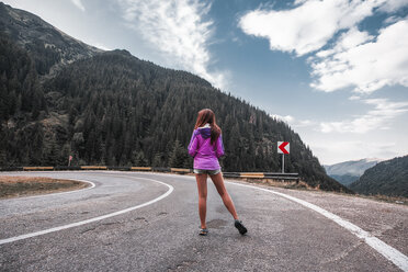 Young woman standing on mountain road with hairpin bend, Draja, Vaslui, Romania, rear view - ISF01403