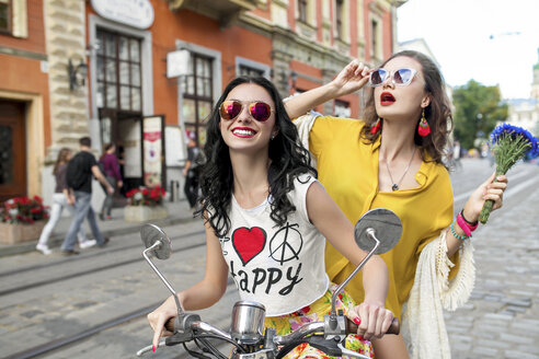 Porträt von zwei glücklichen Freundinnen mit Sonnenbrillen beim Rollerfahren auf einer gepflasterten Straße, Odessa, Ukraine - ISF01415
