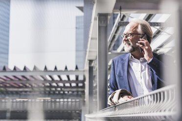 Smiling mature businessman in the city on cell phone - UUF13648