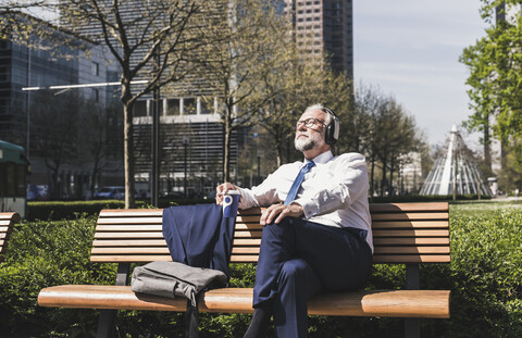 Älterer Geschäftsmann sitzt auf einer Bank und hört Musik, lizenzfreies Stockfoto