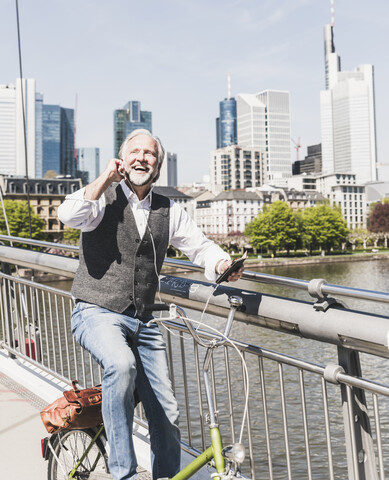 Happy mature man with earbuds, cell phone and bicycle on bridge in the city stock photo