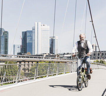 Smiling mature man on bicycle crossing bridge in the city - UUF13705