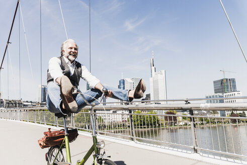 Verspielter reifer Mann auf Fahrrad auf Brücke in der Stadt - UUF13706