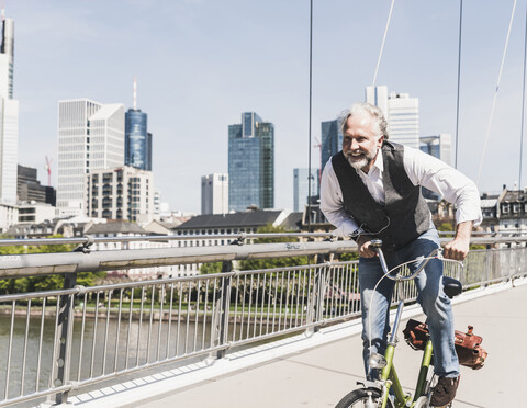 Happy mature man on bicycle crossing bridge in the city stock photo
