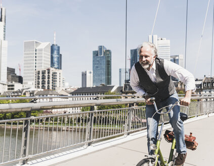 Happy mature man on bicycle crossing bridge in the city - UUF13707