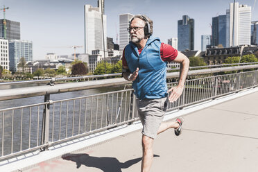 Älterer Mann mit Kopfhörern läuft auf einer Brücke in der Stadt - UUF13719