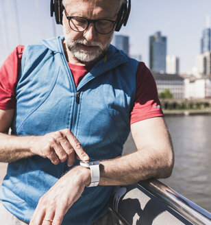 Sportlicher reifer Mann mit Kopfhörern, der sich auf einer Brücke in der Stadt die Zeit nimmt - UUF13720