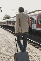 Rear view of mature businessman walking at train platform with suitcase - UUF13731