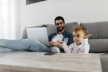 Vater benutzt Laptop zu Hause, Tochter spielt im Vordergrund - JRFF01655