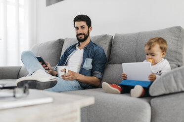 Der Vater arbeitet im Wohnzimmer, während die Tochter das Tablet beobachtet - JRFF01658