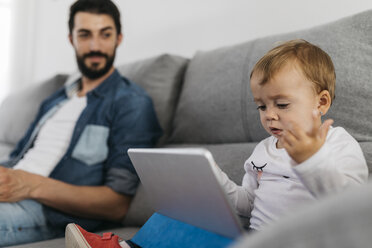 Vater auf der Couch sitzend, während die Tochter das Tablet beobachtet - JRFF01659