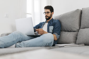 Mann mit Laptop, arbeitet zu Hause auf der Couch - JRFF01662