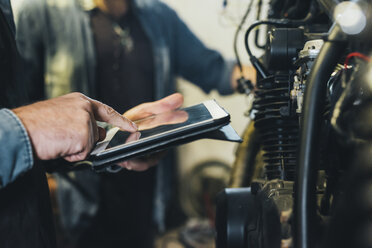 Zwei reife Männer, die in einer Garage arbeiten und ein digitales Tablet benutzen, Nahaufnahme - CUF05701