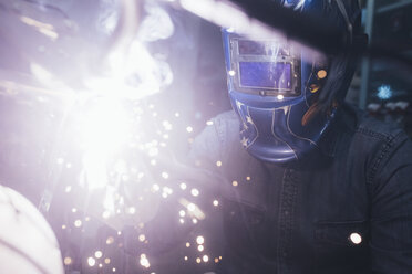 Mature man in garage, working on motorcycle, using welding equipment - CUF05705