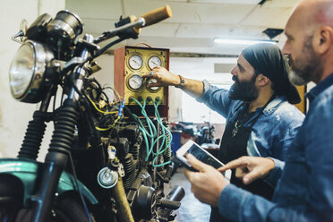 Zwei reife Männer, die in einer Garage an einem Motorrad arbeiten - CUF05707