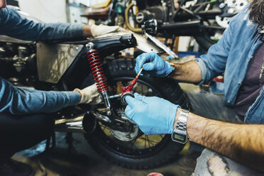 Zwei reife Männer, die in einer Garage an einem Motorrad arbeiten, Nahaufnahme - CUF05710