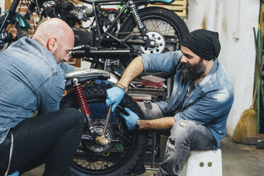 Zwei reife Männer, die in einer Garage an einem Motorrad arbeiten - CUF05711