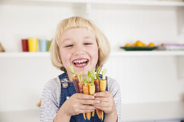 Porträt eines niedlichen Mädchens in der Küche, das ein Bündel bunter Karotten hält - CUF05723