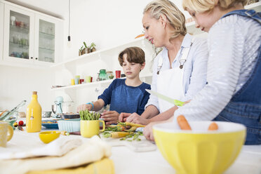 Mature woman preparing vegetables at kitchen table with son and daughter - CUF05730