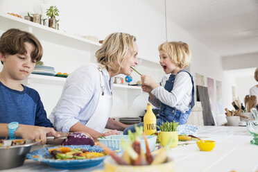 Girl feeding mother asparagus at kitchen table - CUF05731