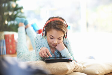 Mädchen liegt auf dem Wohnzimmerboden und schaut auf ein digitales Tablet zu Weihnachten - CUF05738