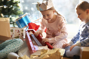 Mädchen und Bruder auf dem Wohnzimmerboden mit Blick auf Spielzeuggitarre Weihnachtsgeschenk - CUF05740