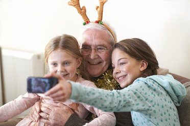 Sisters taking smartphone selfie with grandfather in reindeer antlers - CUF05747