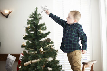 Junge steht auf einem Stuhl, um einen Stern auf den Weihnachtsbaum zu setzen - CUF05751