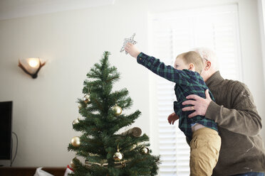 Älterer Mann hebt seinen Enkel hoch, um einen Stern auf den Weihnachtsbaum zu setzen - CUF05752