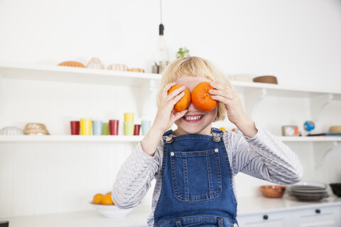 Porträt eines niedlichen Mädchens in der Küche, das sich Orangen vor die Augen hält, lizenzfreies Stockfoto